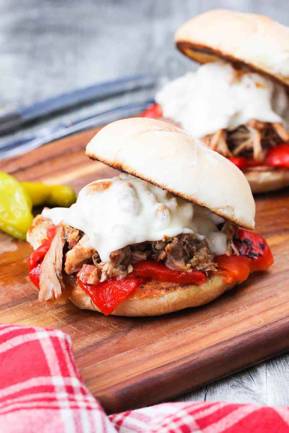 Instant Pot Italian Pulled Chicken Sandwich on a wooden cutting board with a knife and fork next to a patterned red napkin