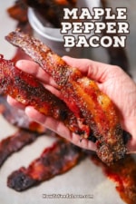 A person holding two strips of maple pepper bacon in the palm of his hand.