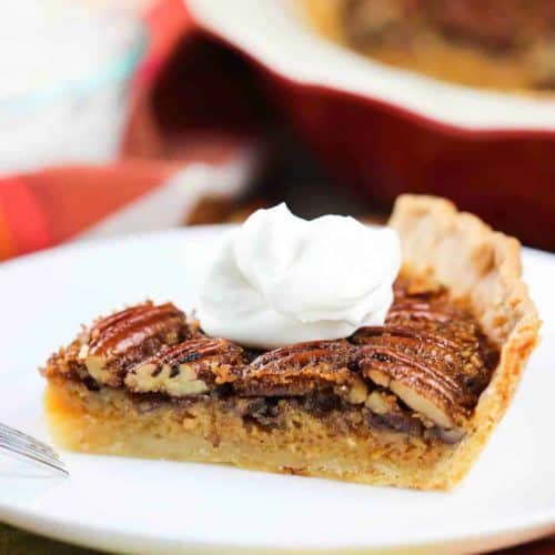 A slice of Classic Pecan Pie topped with whipped cream on a white plate