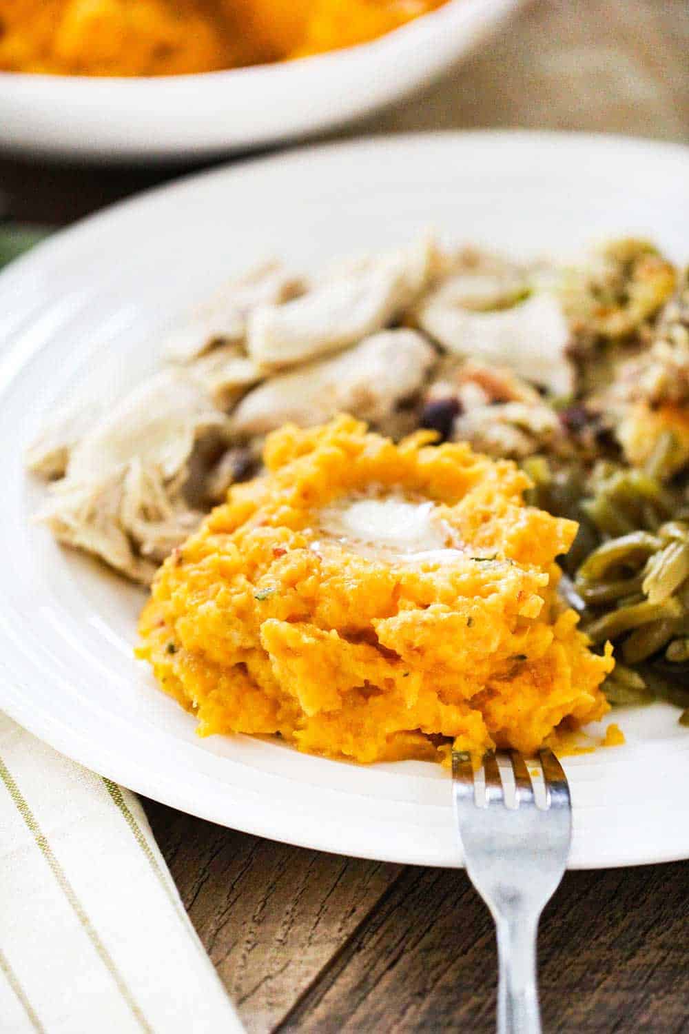 A plate of mashed butternut squash topped with butter, next to roasted turkey, stuffing and green beans. 