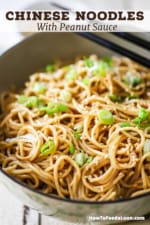 A close-up view of an Asian-style bowl filled with Chinese noodles with peanut sauce and topped with chopped scallions and sesame seeds.
