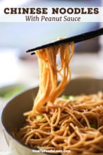 A person using a pair of chopsticks to lift up strands of cooked lo mein in a peanut sauce from a bowl.