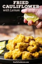 A person squeezing a lemon wedge over black circular plate filled with fried cauliflower and lemon wedges.