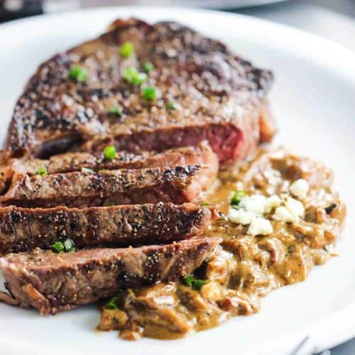 Ribeye with Gorgonzola and Caramelized Onion Sauce on a white plate next to a fork and knife