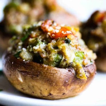 A close-up view of a sausage-stuffed mushroom on a white plate.