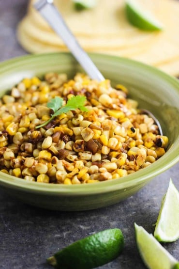 Roasted Corn salsa in a green bowl next to sliced limes