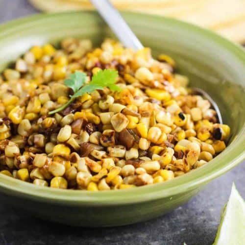 Roasted Corn salsa in a green bowl next to sliced limes