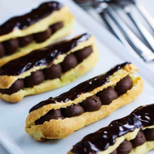 Chocolate Eclairs on a white plate next to silver forks