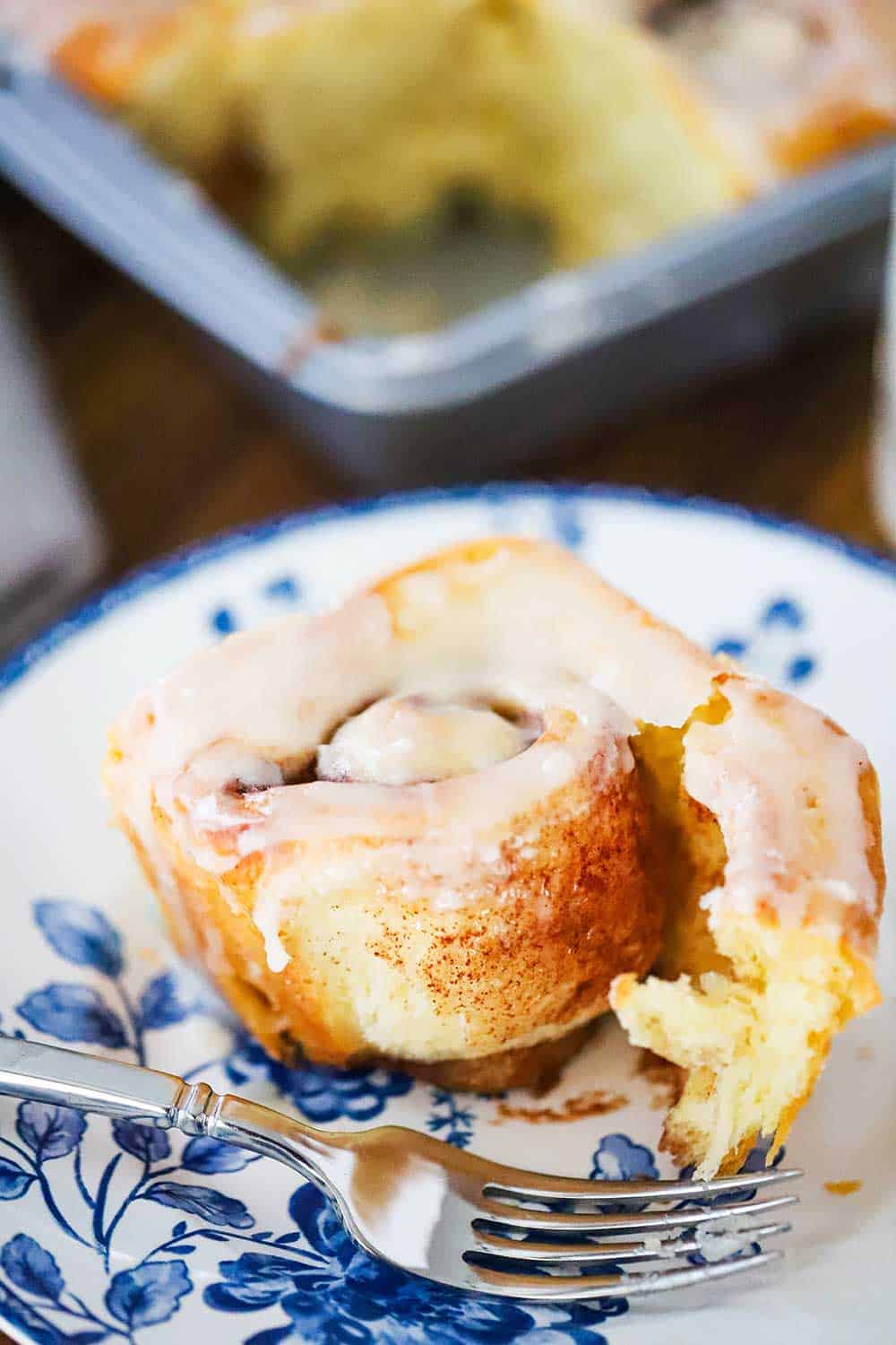 A half-eaten homemade cinnamon roll on a blue-patterned plate with a fork next to it. 