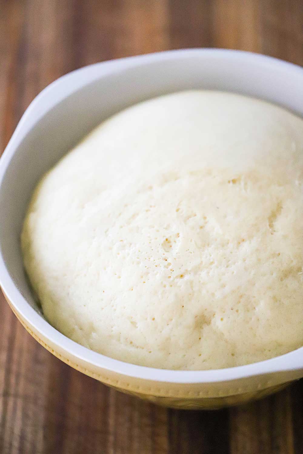  A large ceramic bowl filled with dough that has risen to the top of the sides of the bowl. 