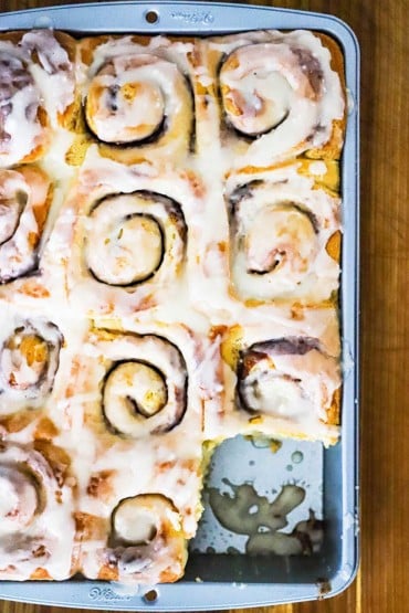 A 9 by 13-inch metal baking pan filled with homemade cinnamon rolls with one in the lower right corner missing.