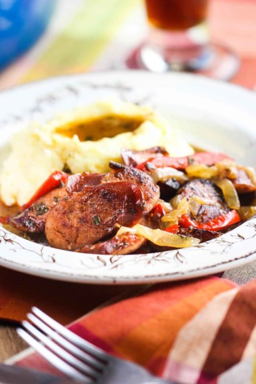 A bowl of Beer-Braised Kielbasa with Peppers next to a patterned napkin and fork