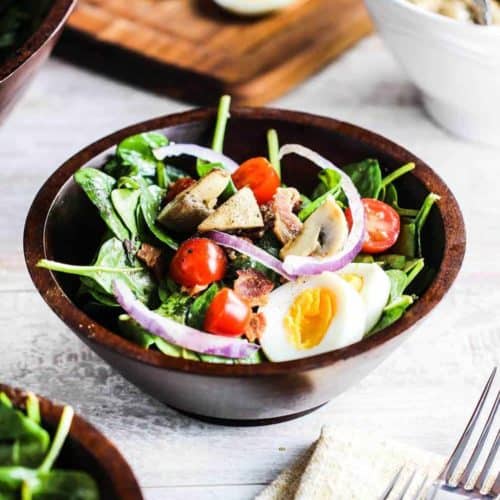 Warm Spinach and Bacon Salad in a bowl next to two forks on top of a beige napkin