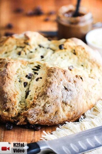 A loaf of Irish Soda Bread sitting on a carving board with a large knife next to it.