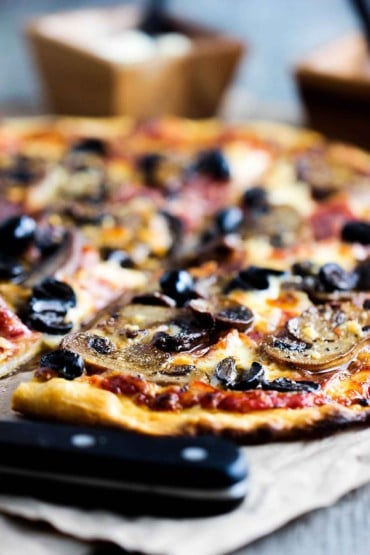 A close-up view of a soppressata, mushroom, and black olive pizza. 
