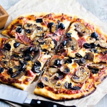 A close-up view of a soppressata, mushroom, and black olive pizza.