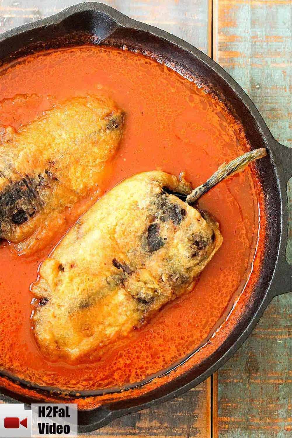 Two Chile rellenos in a red sauce in a cast iron skillet