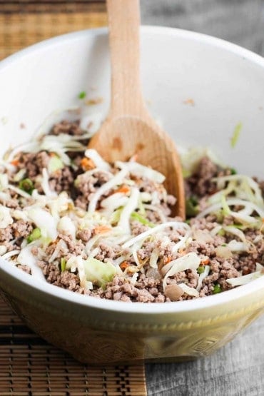 A bowl of egg roll filling being mixed with a wooden spoon