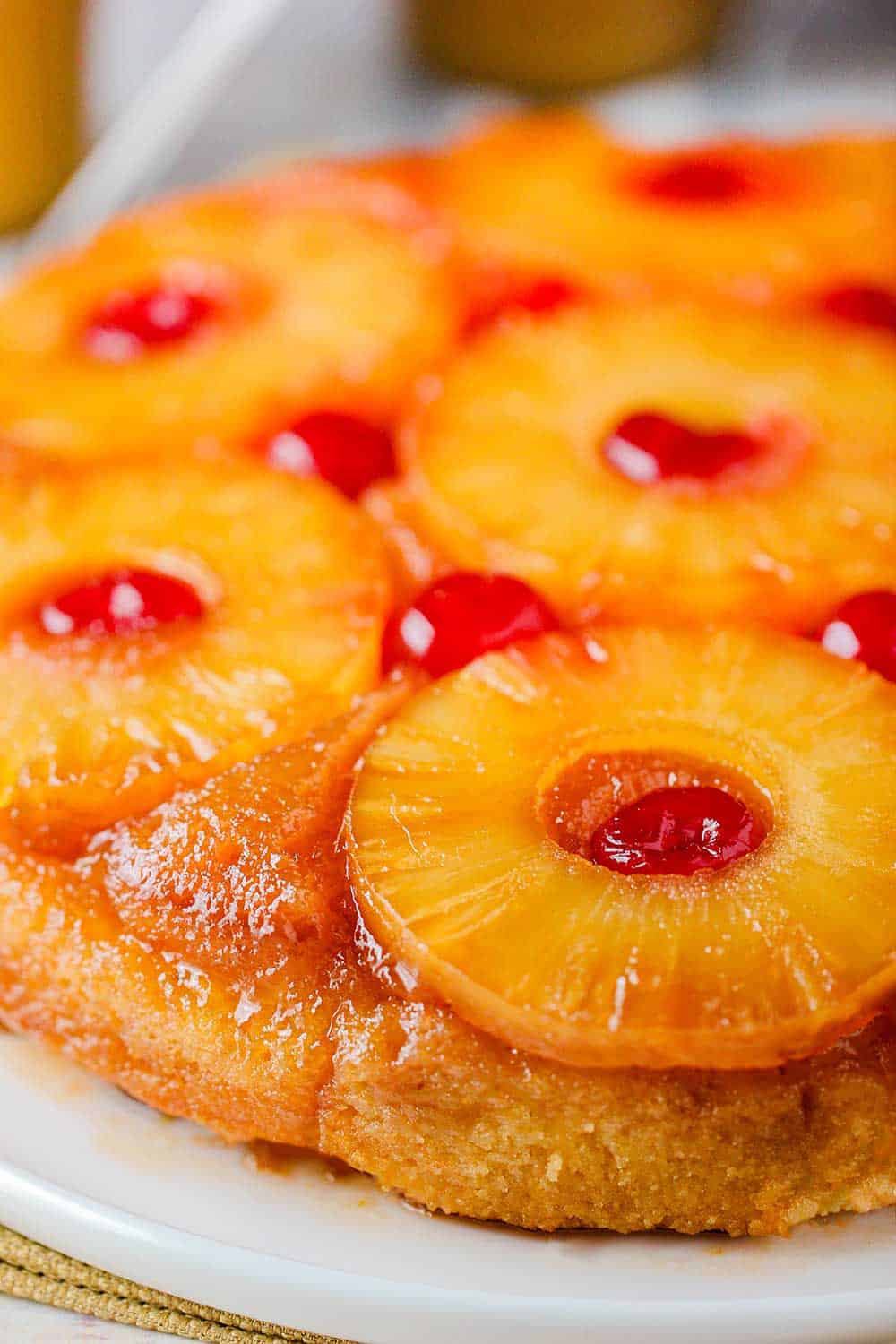 A close up view of a pineapple upside-down cake on a white platter. 