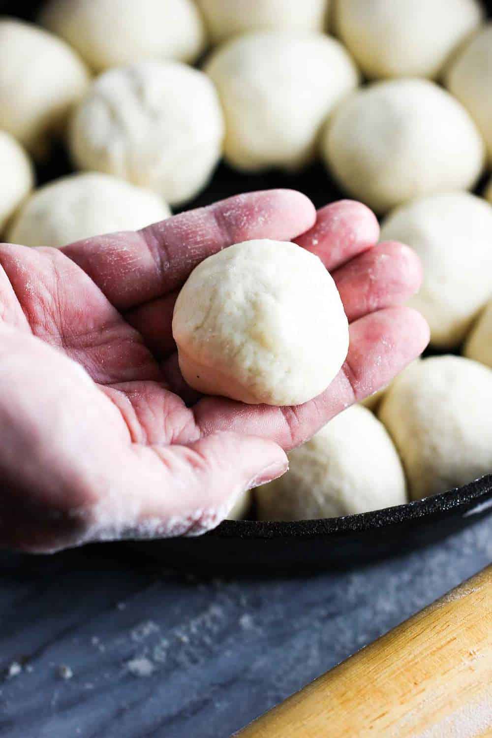 roll dough in a hand over a skillet of other rolled rolls for cheesy skillet rolls