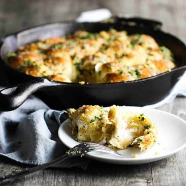 Cheesy skillet roll in a cast iron skillet with one on a plate in front.