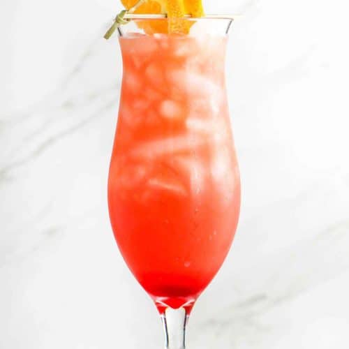 A hurricane cocktail in a tall glass with cherry and orange slice on top.