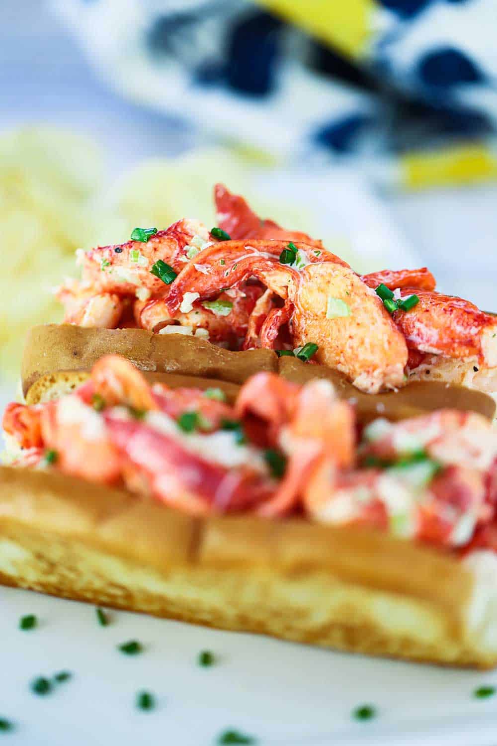 A close-up side view of two lobster rolls on toasted buns with snipped chives sprinkled over the tops. 