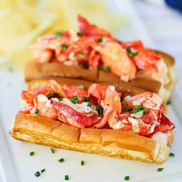 Two lobster rolls sitting on a rectangular white plate with snipped chives sprinkled over the top.