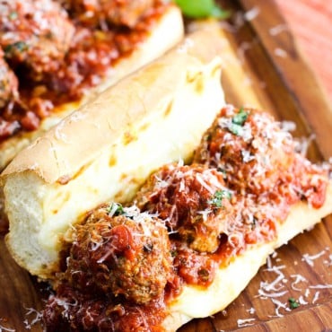 A close-up view of a meatball sub sandwich on a small wooden cutting board.