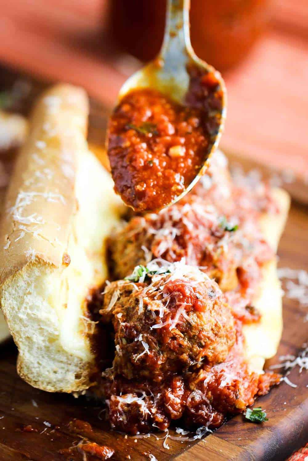 Homemade Italian meatball sub with a spoon pouring marinara over the top. 