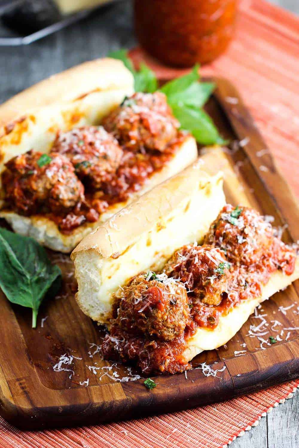 Two freshly made meatball subs on a cutting board with basil nearby.