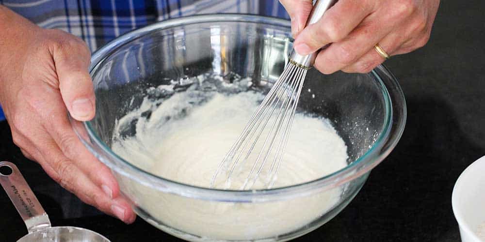 Two hands holding a bowl and whisking a batch of vanilla sauce . 