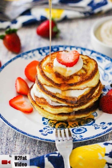 An antique plate holding ricotta pancakes with a strawberry on top and syrup being poured on top.