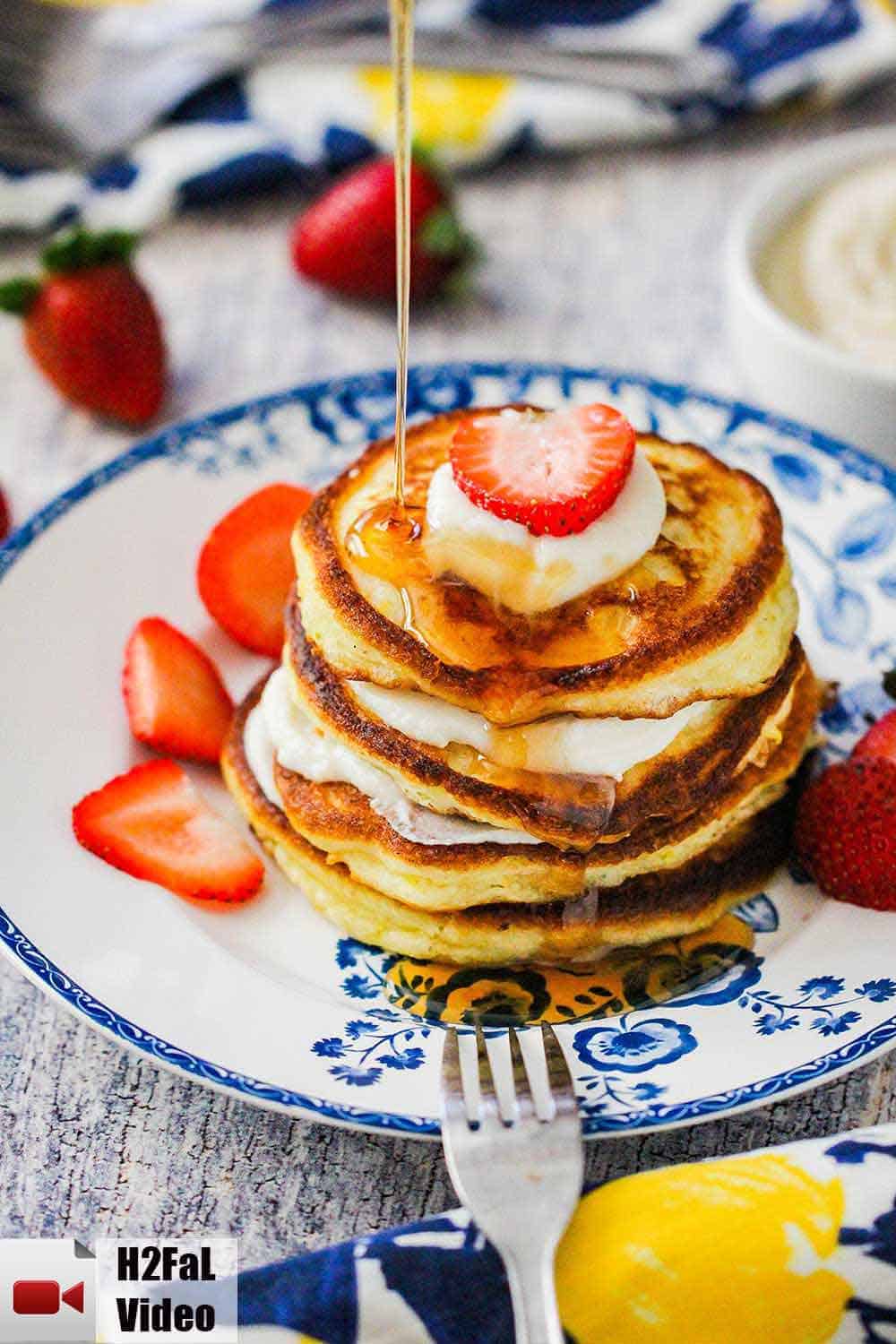 An antique plate holding ricotta pancakes with a strawberry on top and syrup being poured on top. 