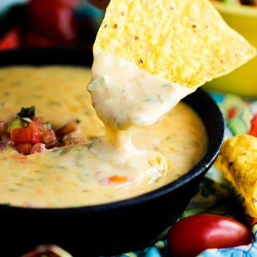 A corn tortilla chip dipped into a bowl of creamy Tex-Mex queso.