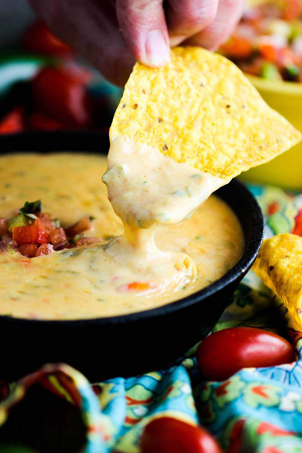 A corn tortilla chip dipped into a bowl of creamy Tex-Mex queso. 