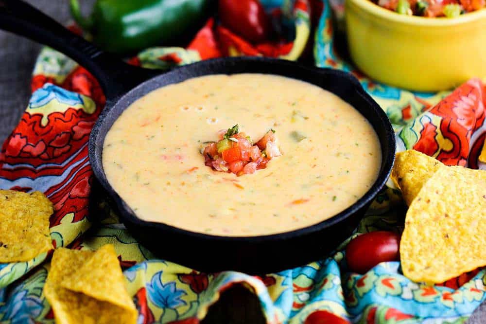 A skillet full of Tex-Mex queso cheese dip with tomatoes and peppers sprinkled on top. 