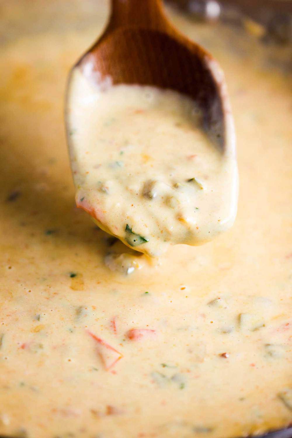 A wooden spoon lifting up a spoonful of classic Tex-Mex Queso cheese dip. 