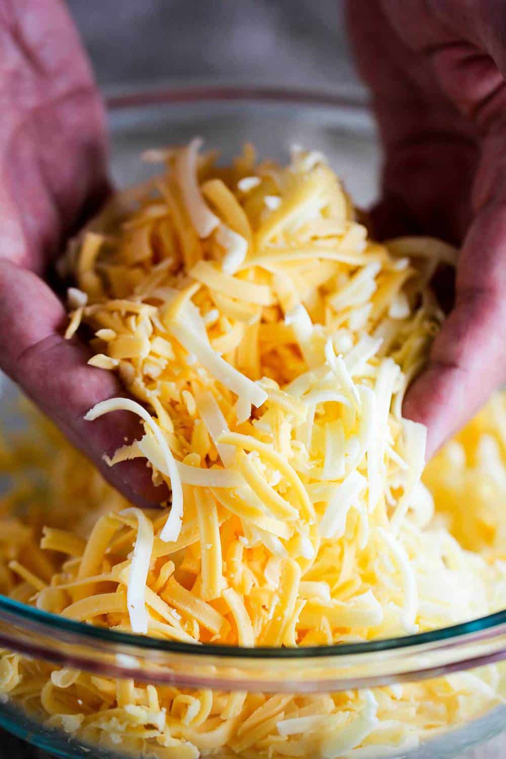 Shredded yellow and white American cheese being lifted out of a glass bowl. 