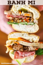 A person holding a banh mi sandwich that has been sliced in half so the components of the sandwich are visible including pork, vegetables, and herbs.