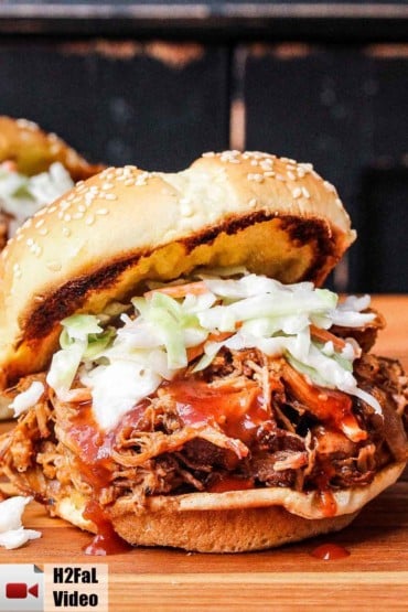 Slow-cooker pulled pork sandwich topped with coleslaw on a wooden cutting board.
