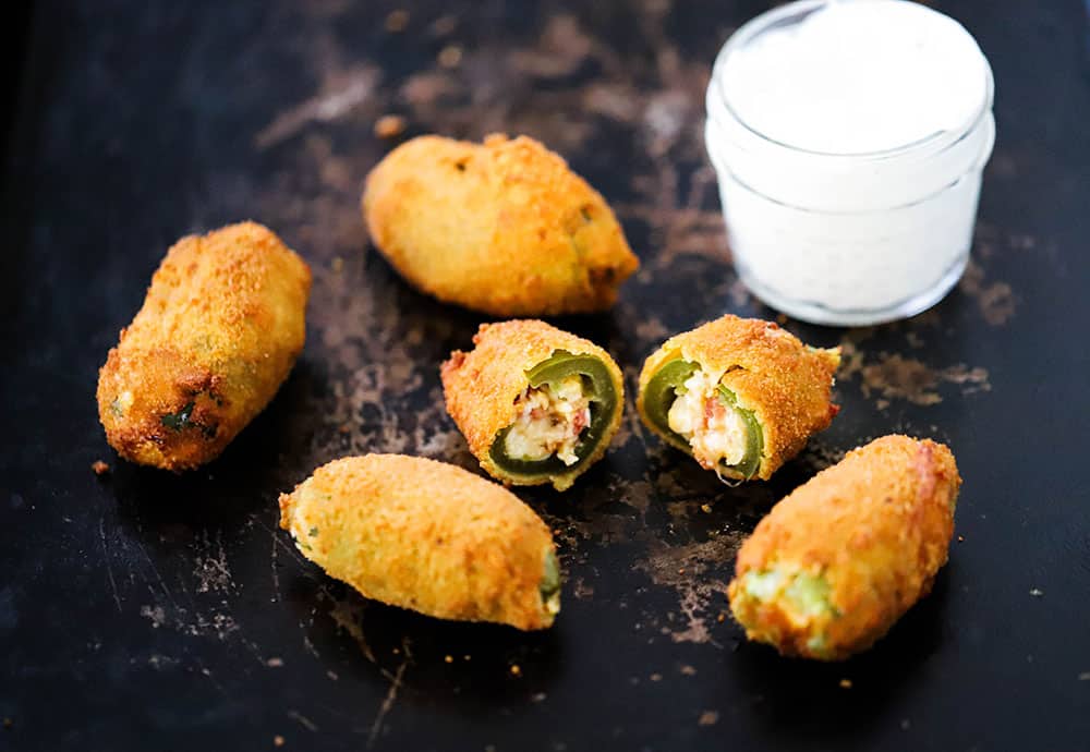 4 jalapeño poppers on a baking sheet with one split open and sitting next to a small jar of sour cream. 