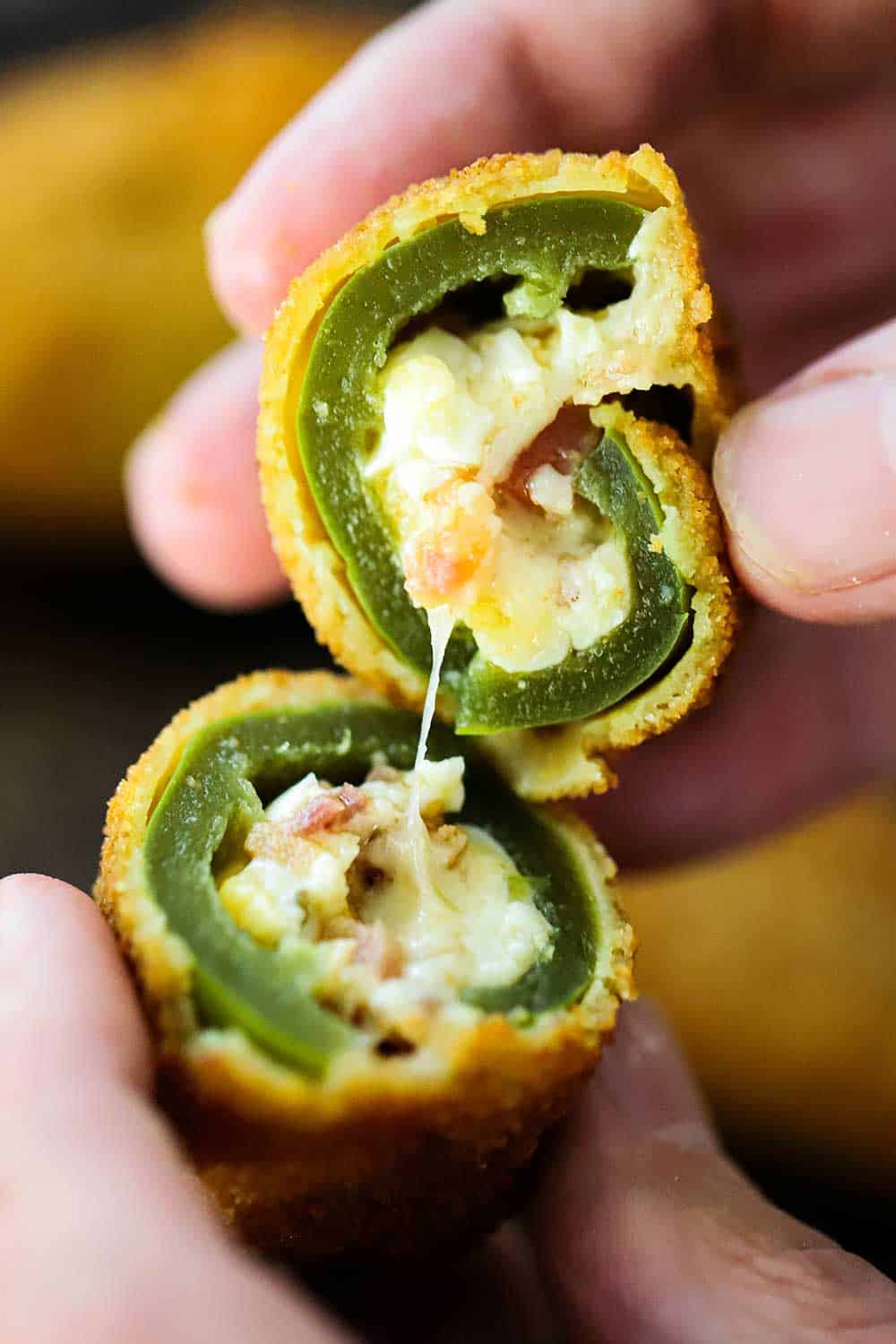 Two hands holding a jalapeño popper that has been split in half showing melted cheese. 