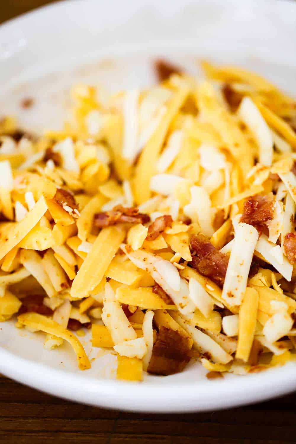 A white bowl filled with shredded cheddar and Monterey Jack cheese and crumbled bacon. 