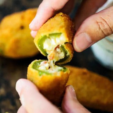 Two hands holding a jalapeño popper that has been split in half showing melted cheese.