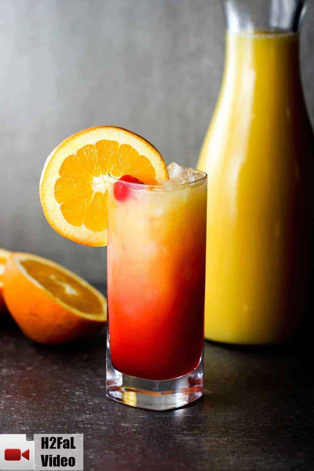 Classic tequila sunrise with an orange and bottle of juice nearby. 