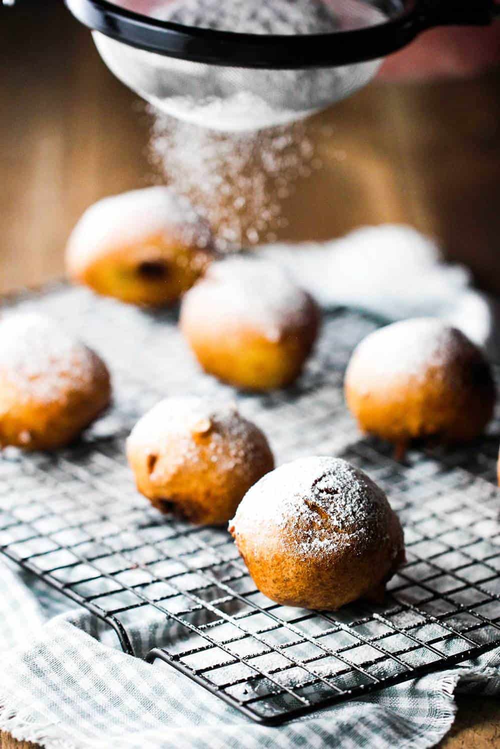 Brownie fritters being sprinkled with sugar on a baking rack