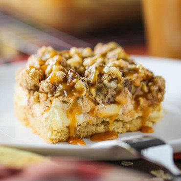 A close-up view of a cream cheese apple bar with pecan streusel topping sitting on a white dessert plate.