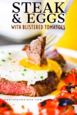 A fork with a piece of steak stuck into it is being plunged into the yolk of an egg sitting on top of a seared steak next to roasted cherry tomatoes.