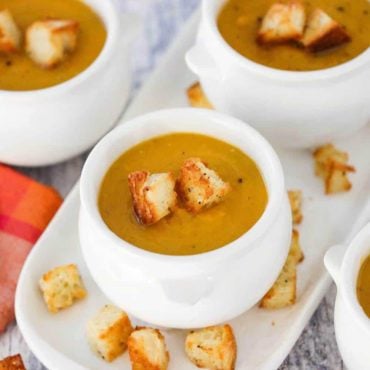 A white crock of roasted butternut squash soup with homemade croutons on and around it.